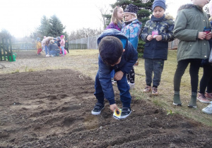 Chłopiec sieje nasiona, dzieci przyglądają mu się z zaciekawieniem.